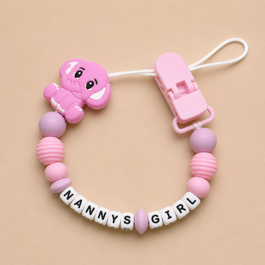 Pink baby dummy clip with 'NANNY'S GIRL' letters on a beige background
