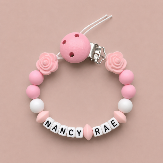 Pink and white baby dummy clip with 'Nancy Rae' on a beige background