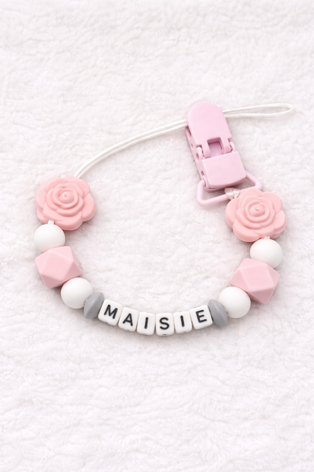 Baby teether with pink and white beads and a clip on a textured white background