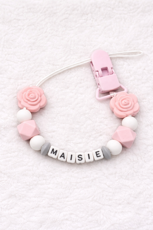 Baby teether with pink and white beads and a clip on a textured white background