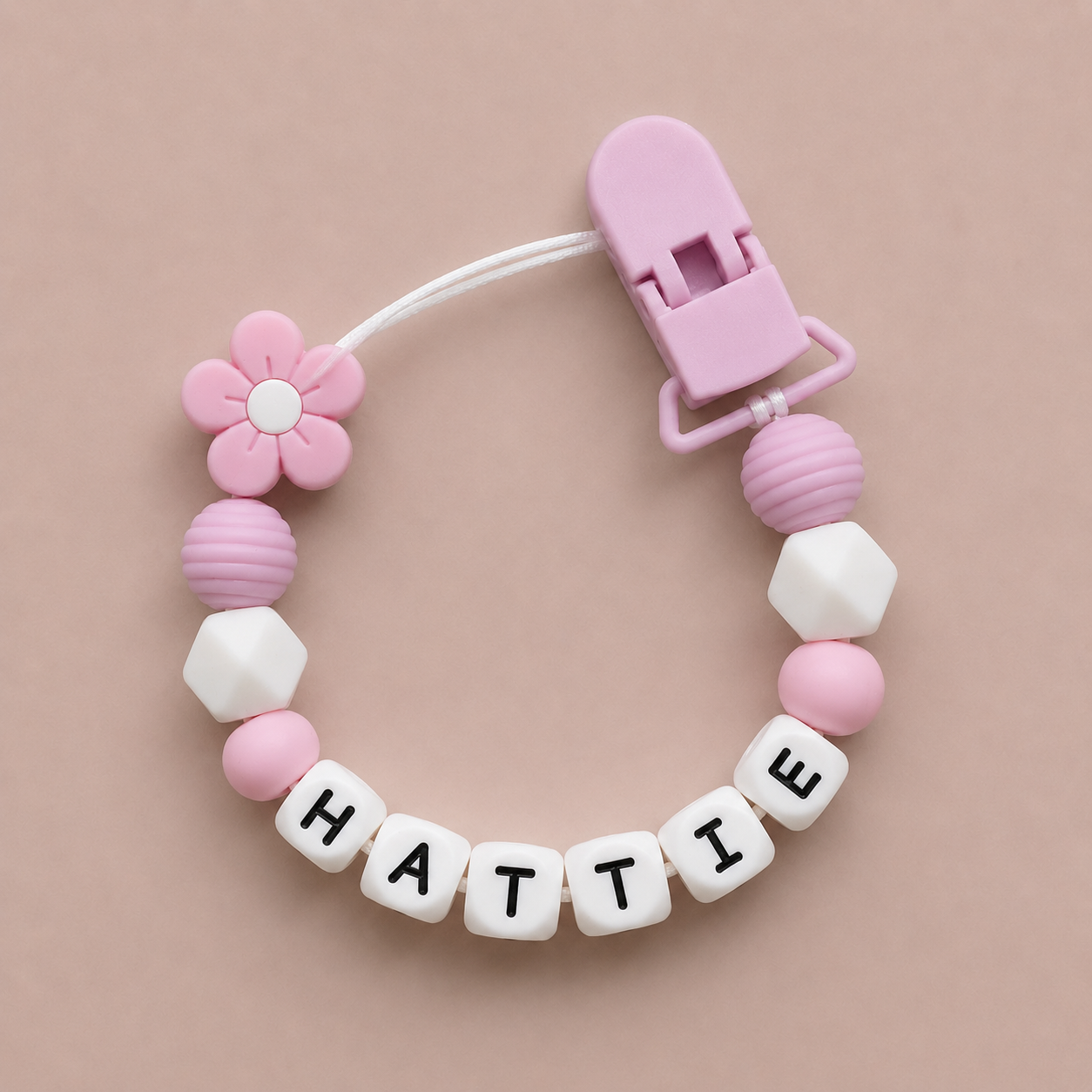 Pink and white dummy clip with 'HATTIE' on a beige background