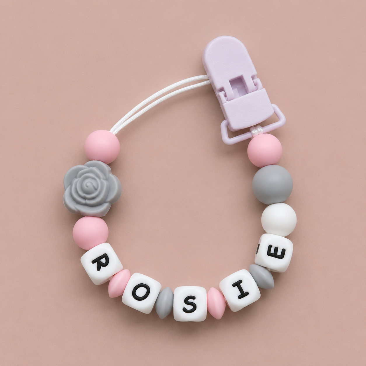 Baby dummy clip with 'ROSIE' beads on a beige background