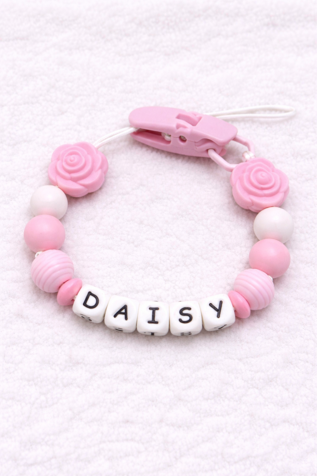 Pink and white teething dummy clip with 'DAISY' on a light pink background
