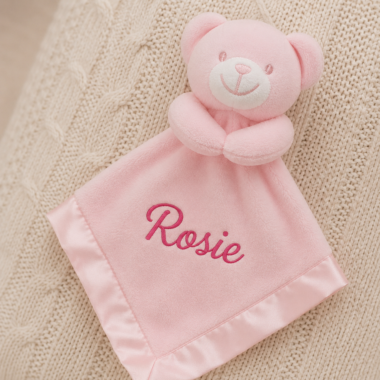 Pink teddy bear security blanket with 'Rosie' embroidered on a textured beige background