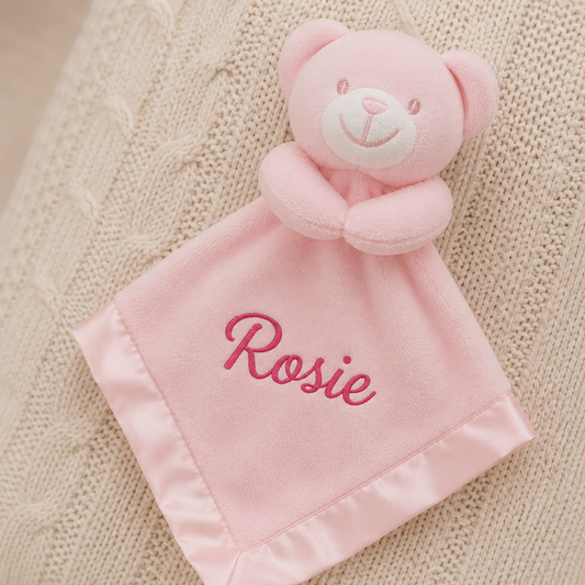 Pink teddy bear security blanket with 'Rosie' embroidered on a textured beige background