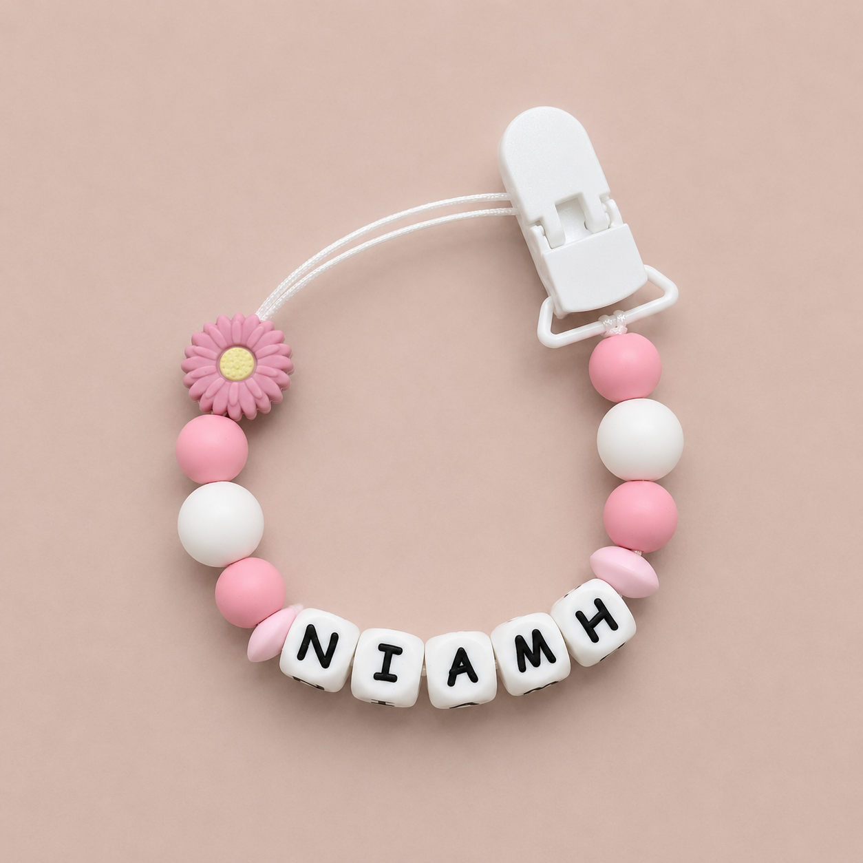 Baby dummy clip with pink and white beads and a clip on a beige background