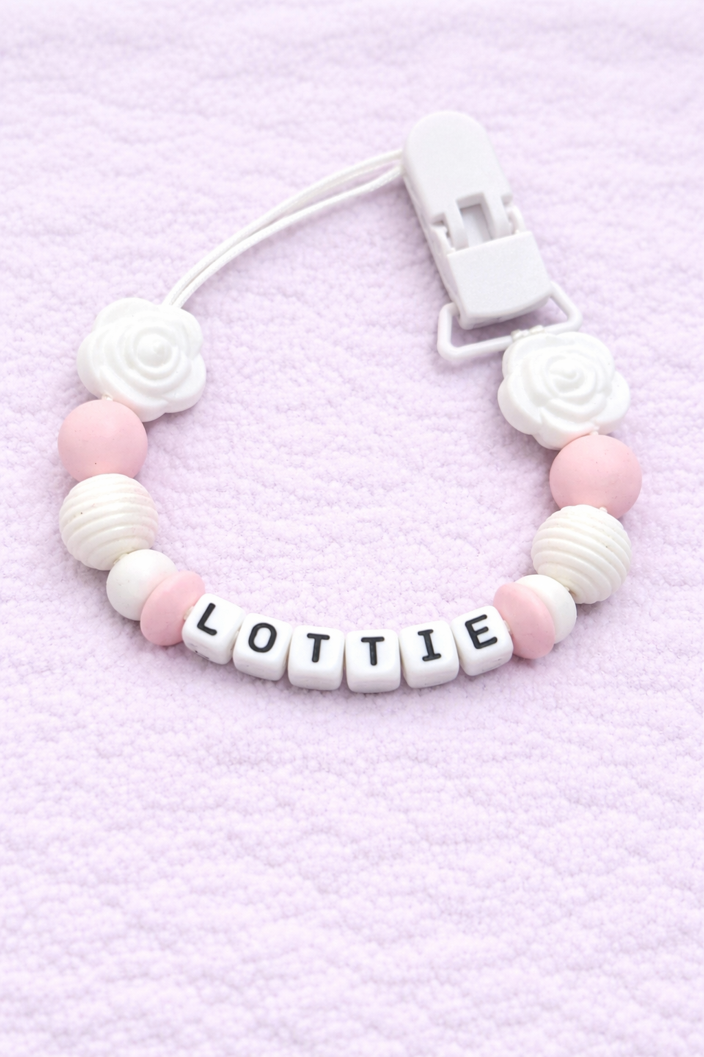dummy clip with pink and white beads and 'LOTTIE' letter beads on a light purple background