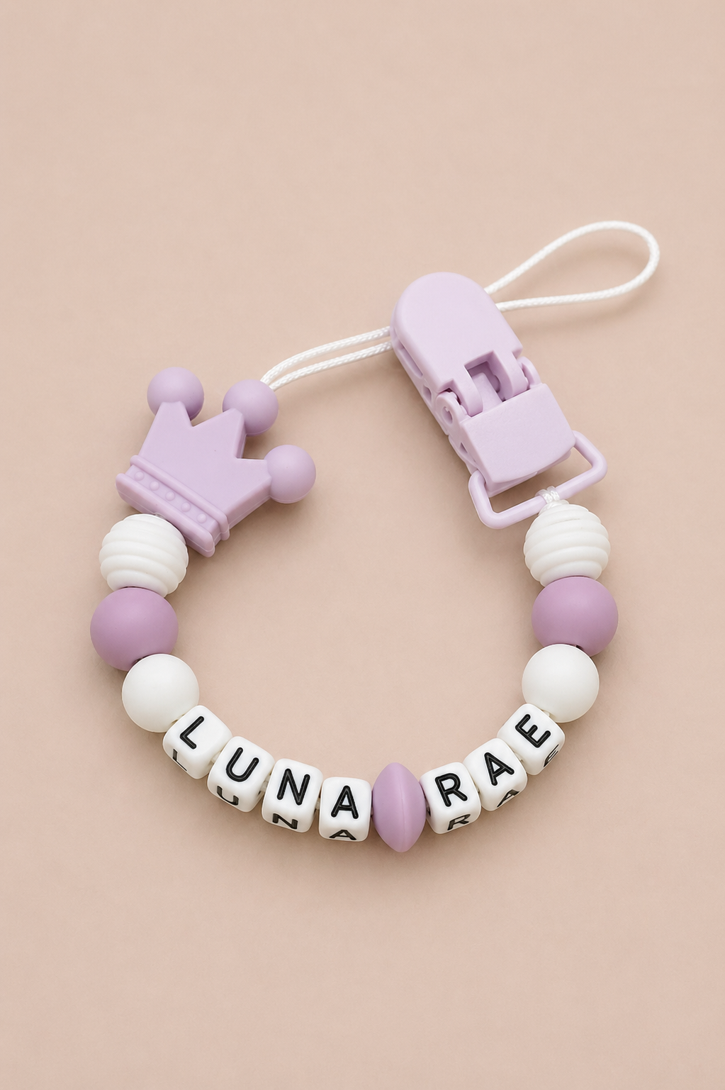 Silicone beaded pacifier clip with crown design and letter beads on a beige background