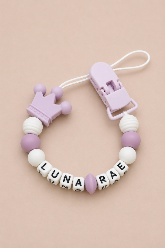 Silicone beaded pacifier clip with crown design and letter beads on a beige background