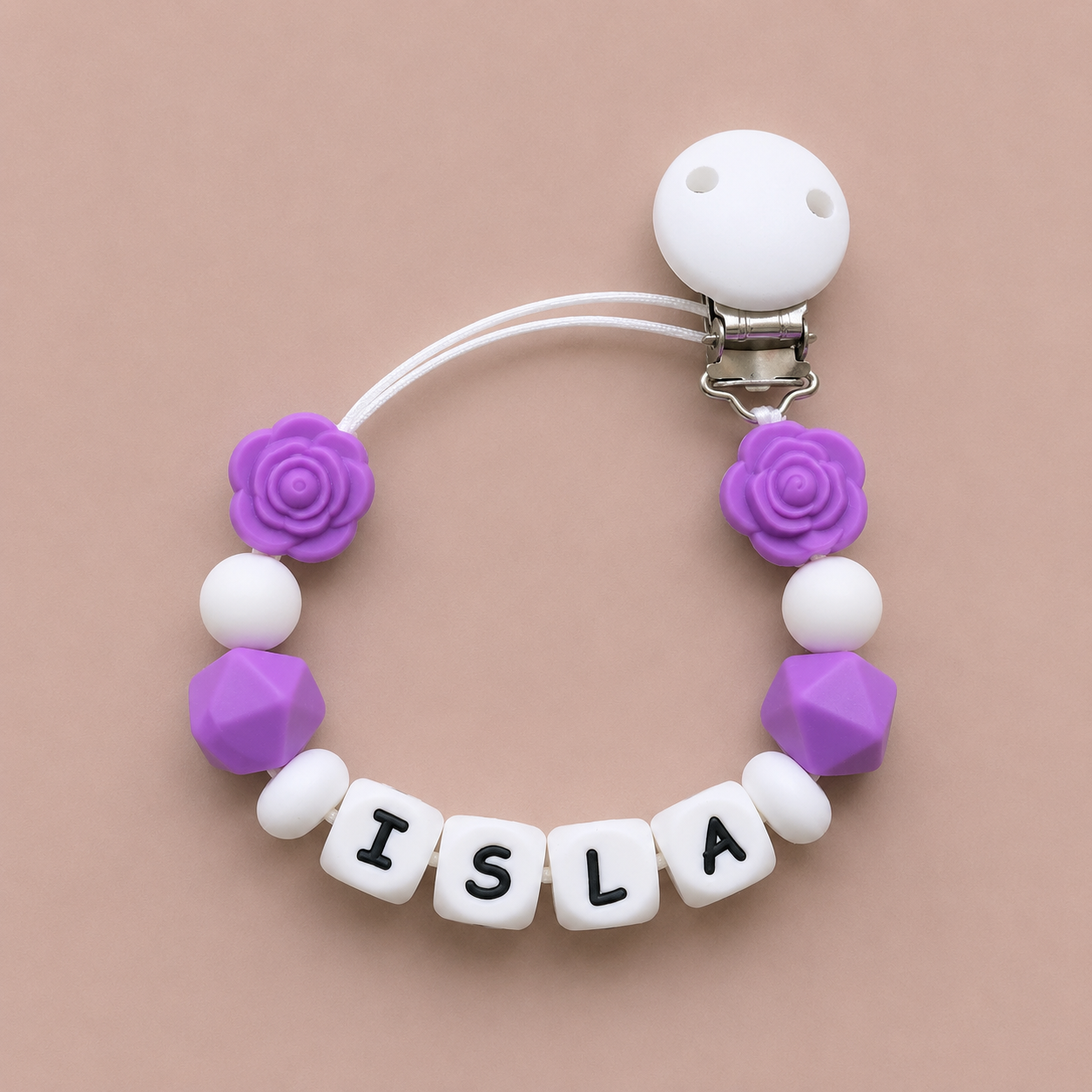 Baby dummy clip with purple and white beads spelling 'ISLA' on a beige background