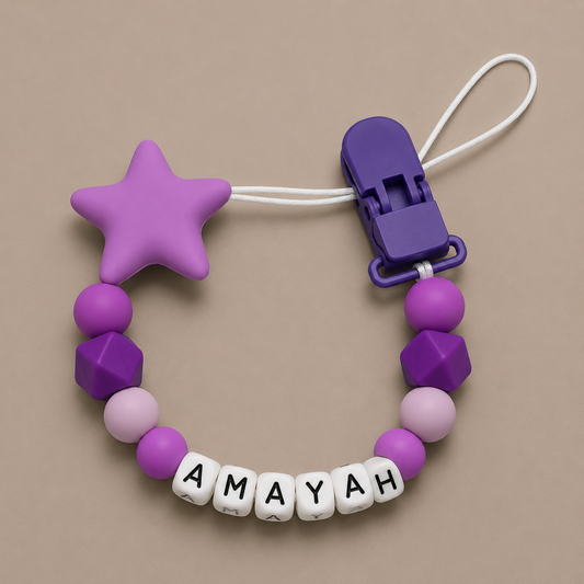 Purple and pink dummy clip with 'AMAYAH' on a beige background