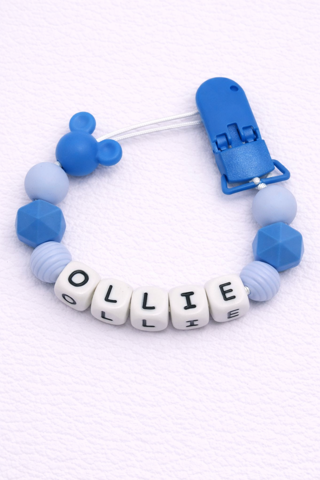 Blue and white pacifier clip with 'OLLIE' on a white background