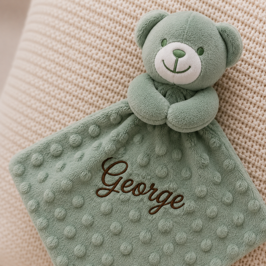 Green teddy bear with a blanket labeled 'George' on a beige background