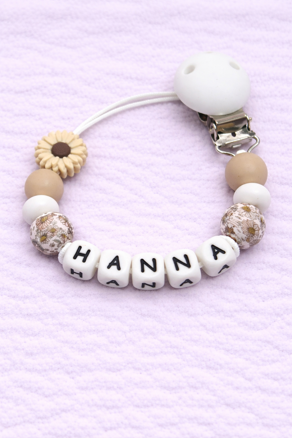 Beaded pacifier clip with 'HANNA' on a light purple background