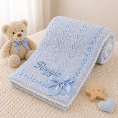 Blue baby blanket with embroidered name, teddy bear, star, and heart toys on a beige surface.