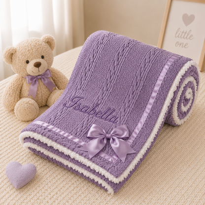 Purple baby blanket with embroidered name, teddy bear, and heart on a beige surface.