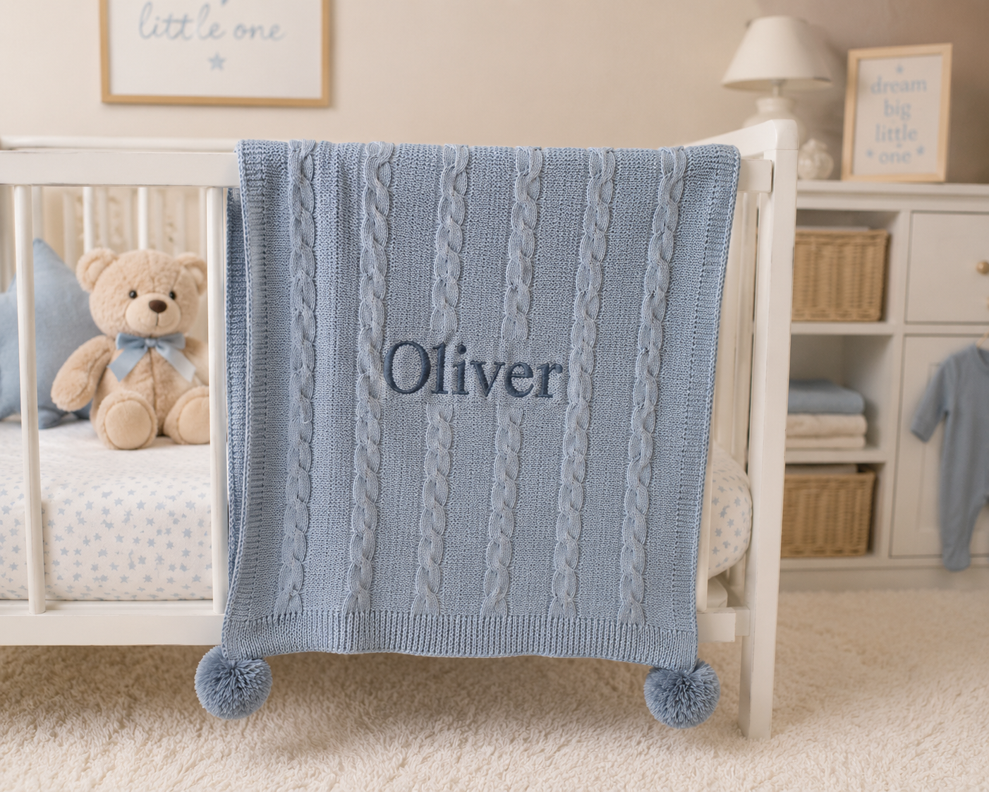 Blue cable knit blanket with 'Oliver' embroidered on a crib in a nursery.