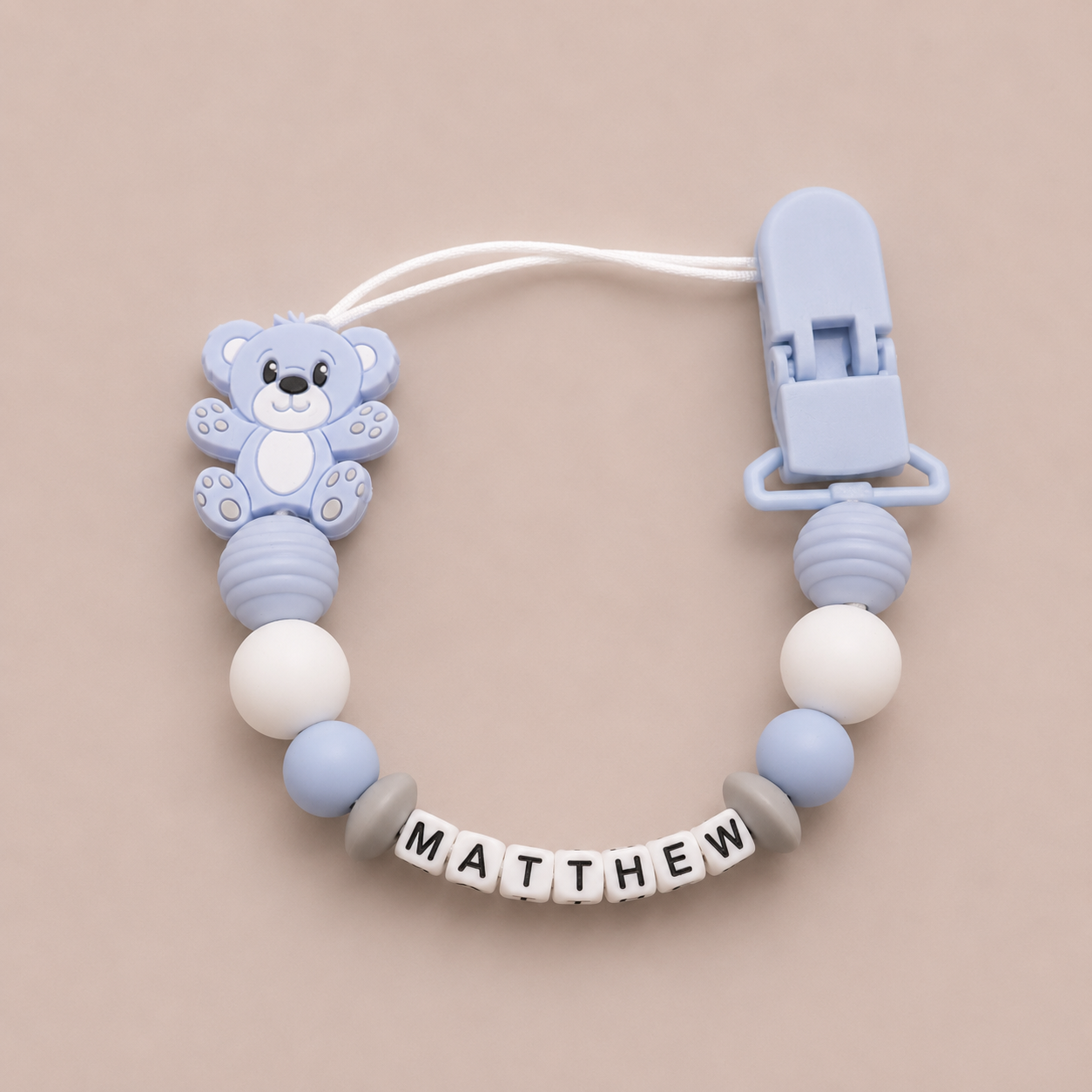 Baby dummy clip with bear design and 'MATTHEW' name on a beige background