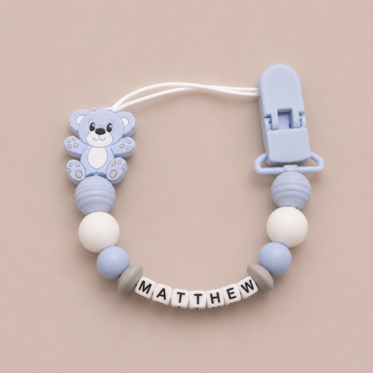 Baby dummy clip with bear design and 'MATTHEW' name on a beige background