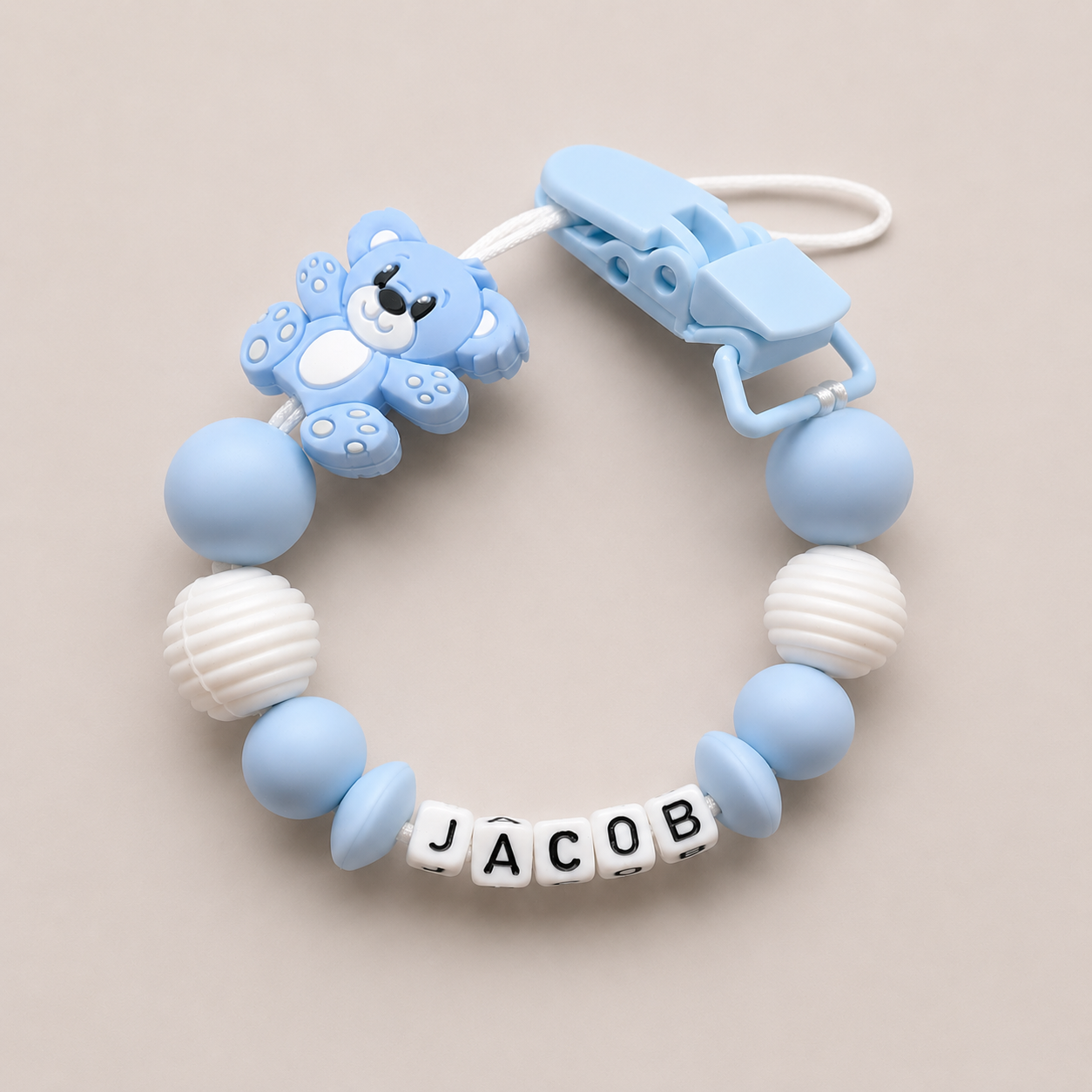 Teething ring with blue and white beads and a bear-shaped clip on a beige background