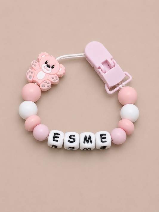 Pink and white dummy clip with 'ESME' on a beige background