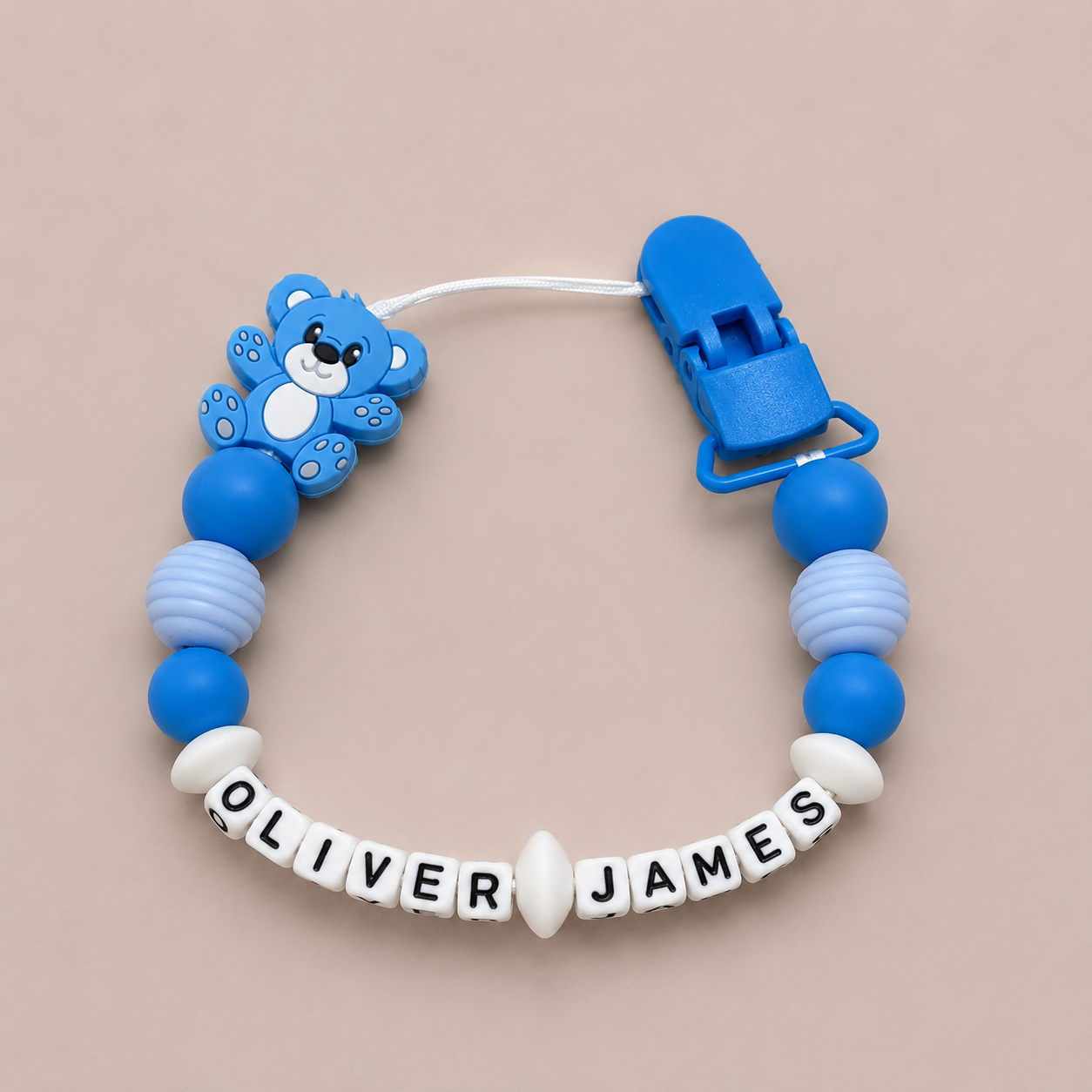 Blue and white pacifier clip with teddy bear design on a beige background