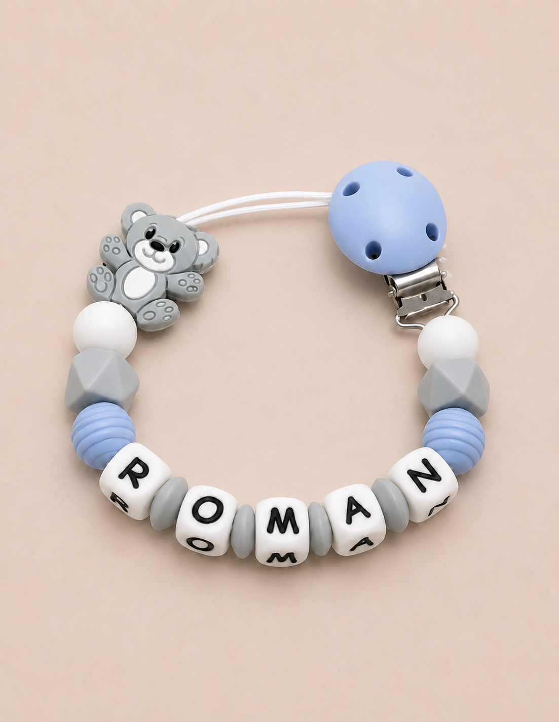 Baby dummy clip with teddy bear charm and name beads on a beige background