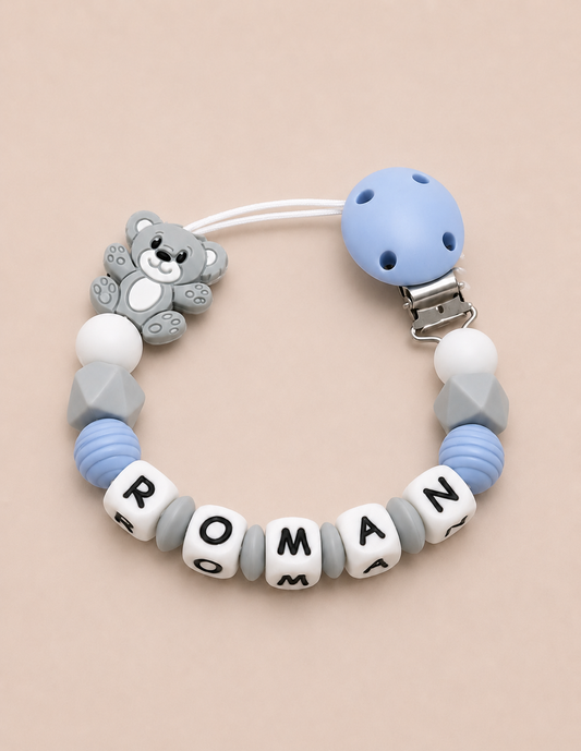 Baby dummy clip with teddy bear charm and name beads on a beige background