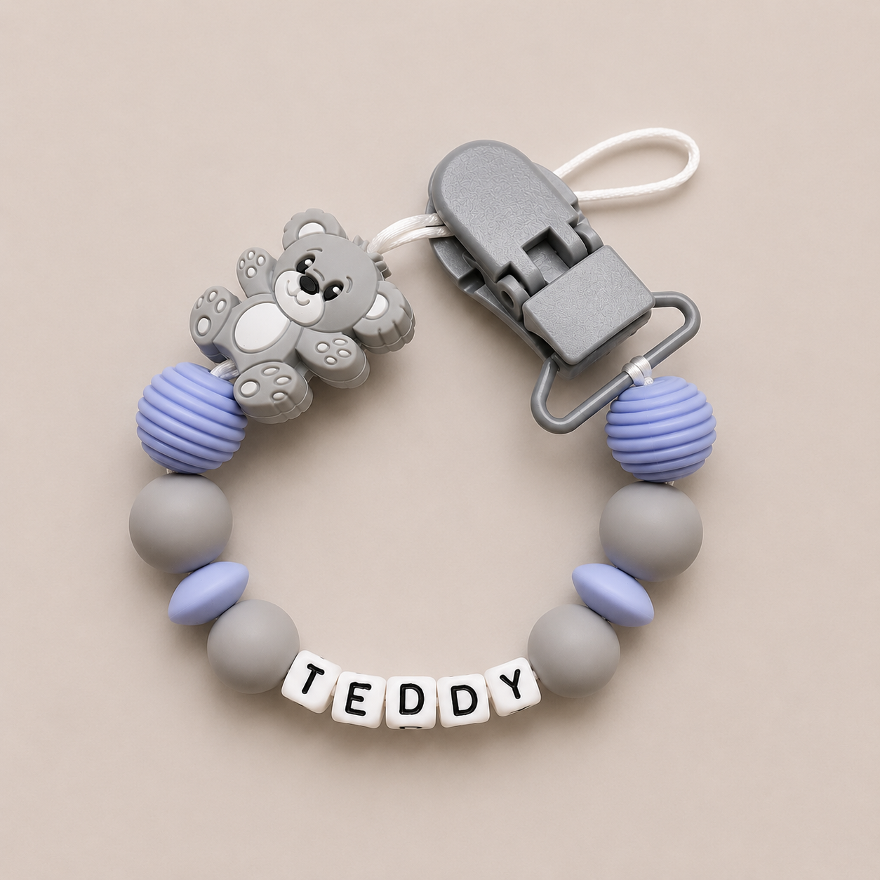 dummy clip with teddy bear attachment and 'TEDDY' beads on a beige background
