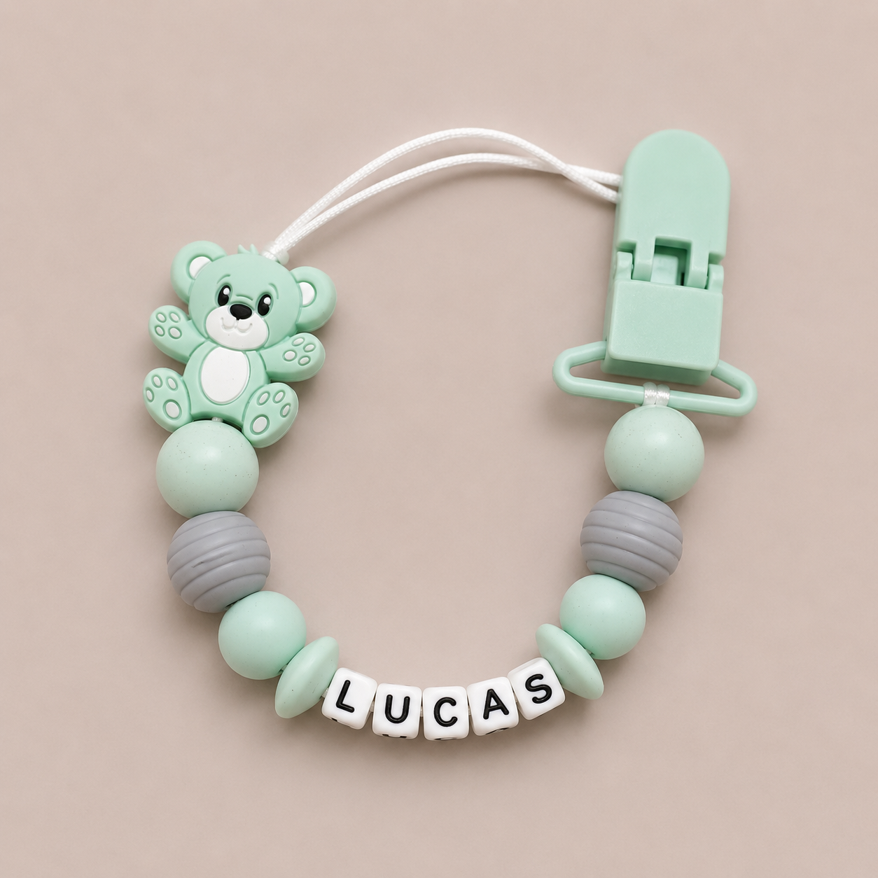 dummy clip with bear design and 'LUCAS' beads on a beige background