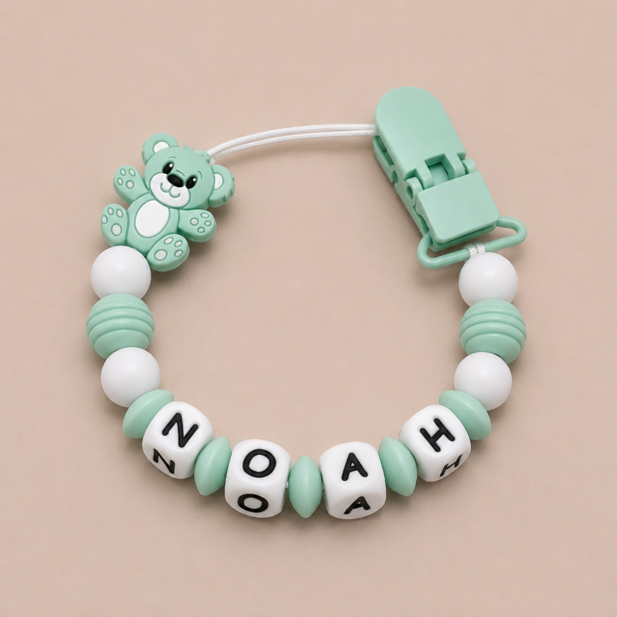 dummy clip with teddy bear design and personalized name beads on a beige background