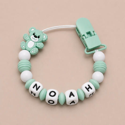 dummy clip with teddy bear design and personalized name beads on a beige background