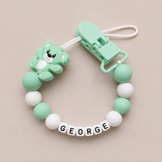 Mint green and white dummy clip with a clip and 'GEORGE' label on a beige background