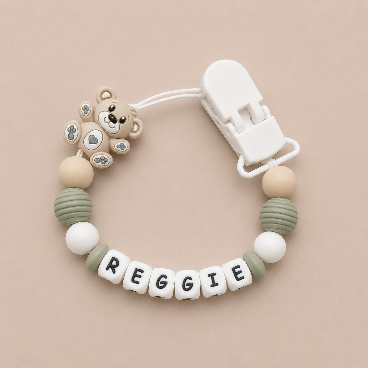 dummy clip with bear design and 'REGGIE' name on a beige background