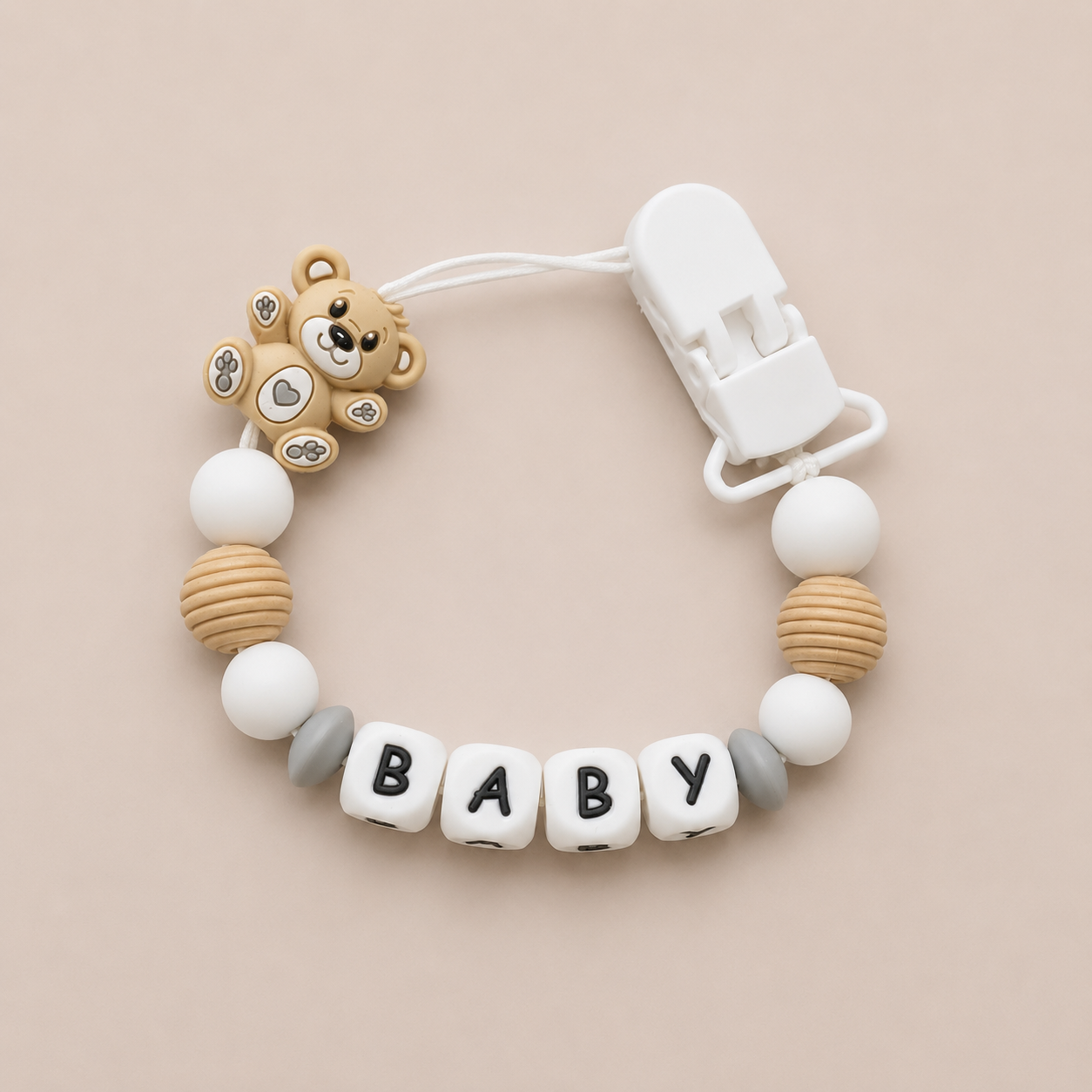 Baby dummy clip with bear charm and 'BABY' beads on a beige background