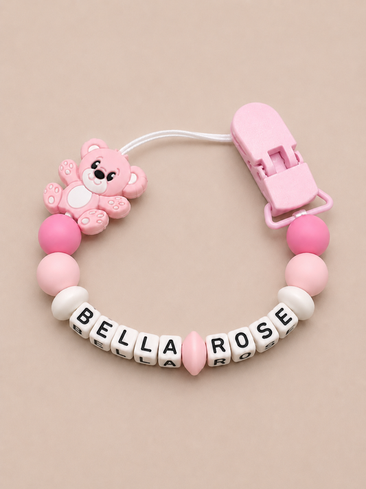 Pink pacifier clip with teddy bear charm and 'Bella Rose' letter beads on a beige background