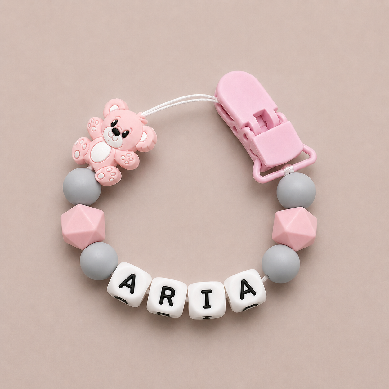 Baby dummy clip with pink bear charm and 'ARIA' letter beads on a beige background