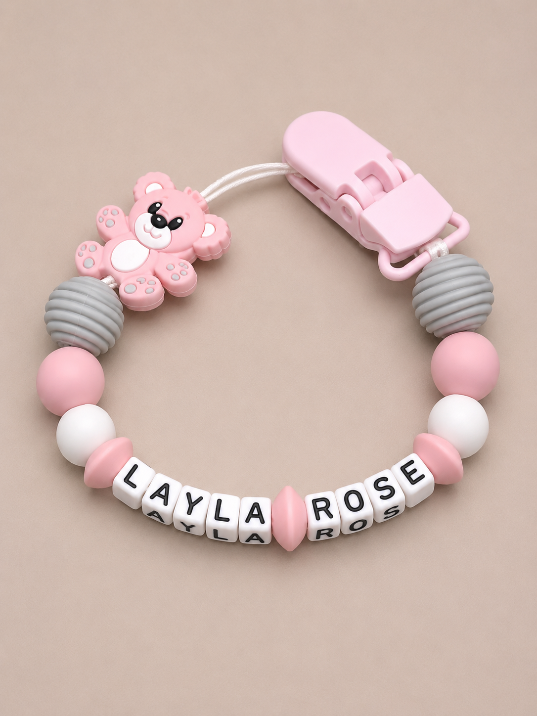 Baby dummy clip with pink and gray beads and a bear-shaped clip on a beige background