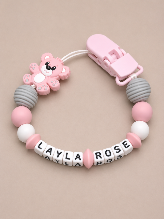 Baby dummy clip with pink and gray beads and a bear-shaped clip on a beige background