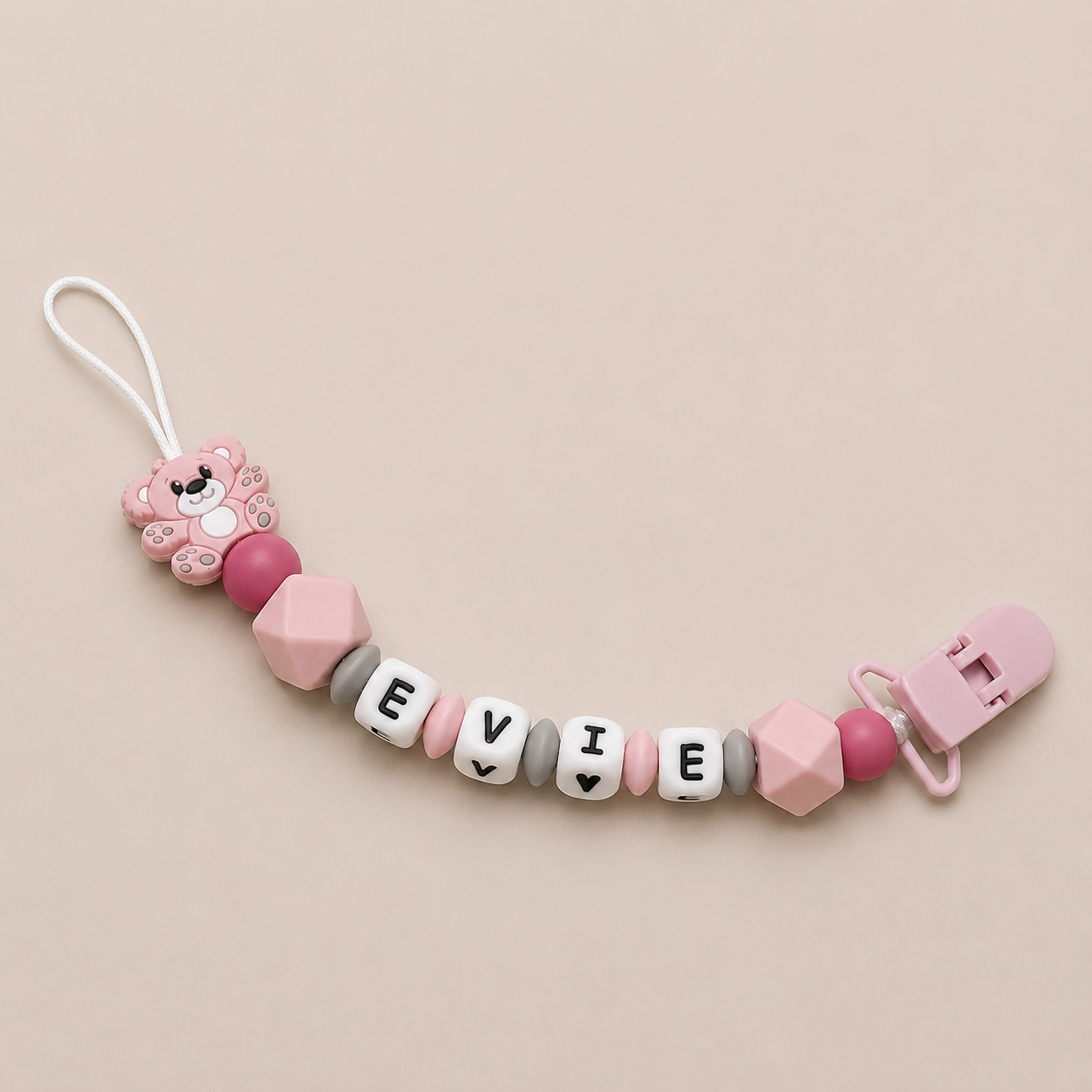 Pink and gray dummy clip with 'EVIE' beads on a beige background