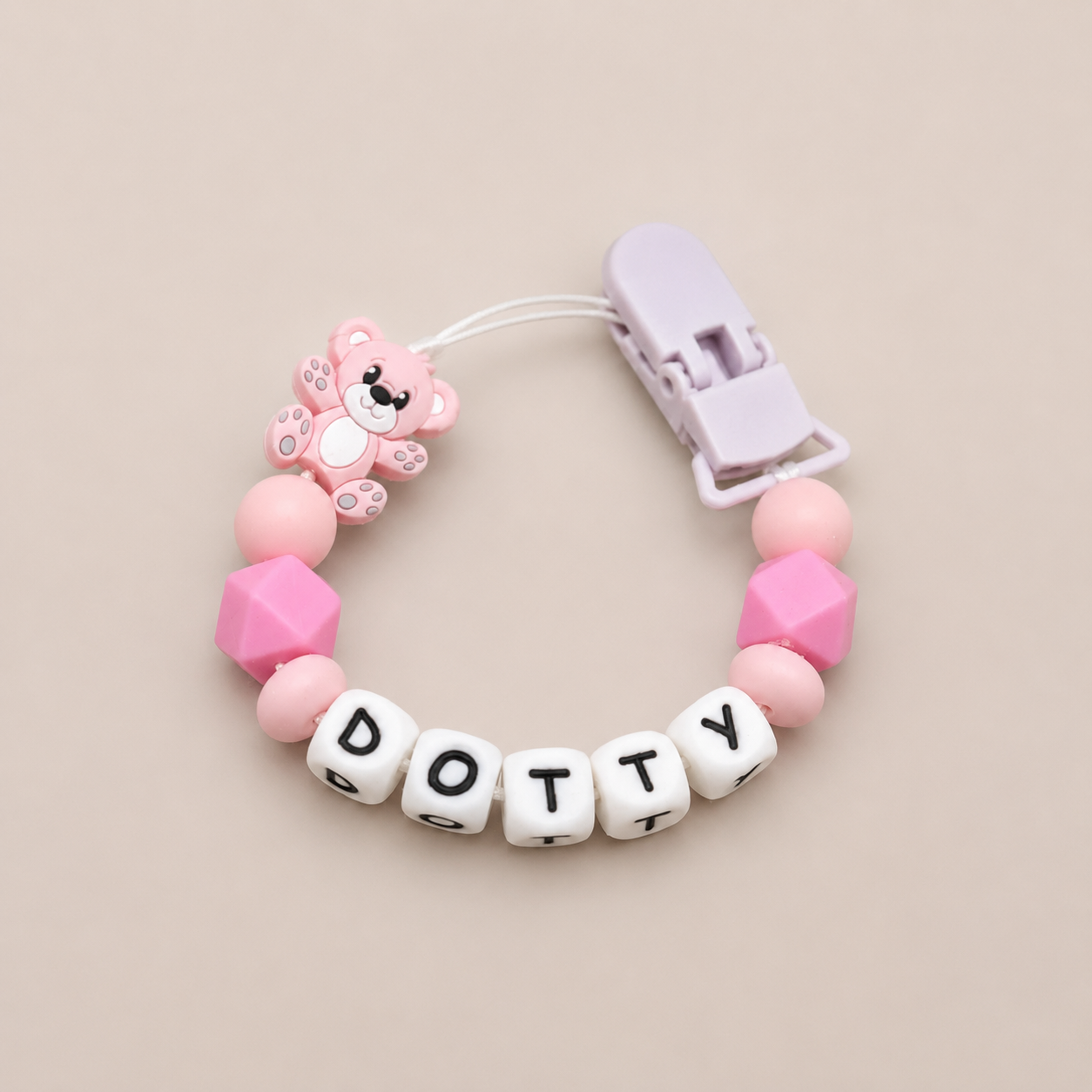 Pink and white pacifier clip with 'Dotty' letters on a beige background