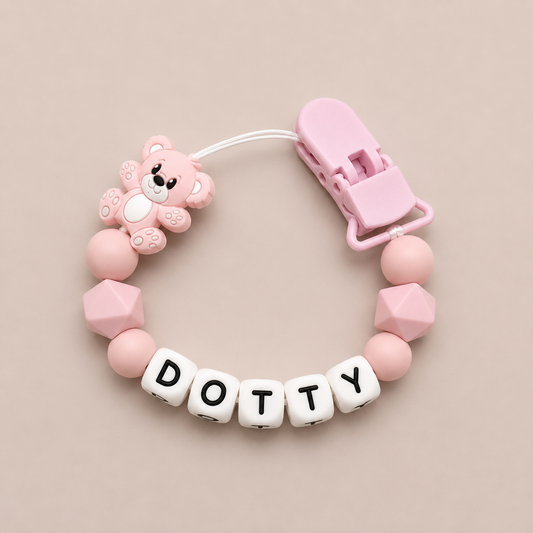 Pink dummy clip with bear design and 'Dotty' letter beads on a beige background