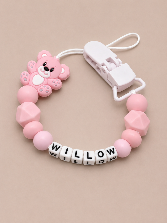 Pink baby dummy clip with a bear charm and 'WILLOW' beads on a beige background