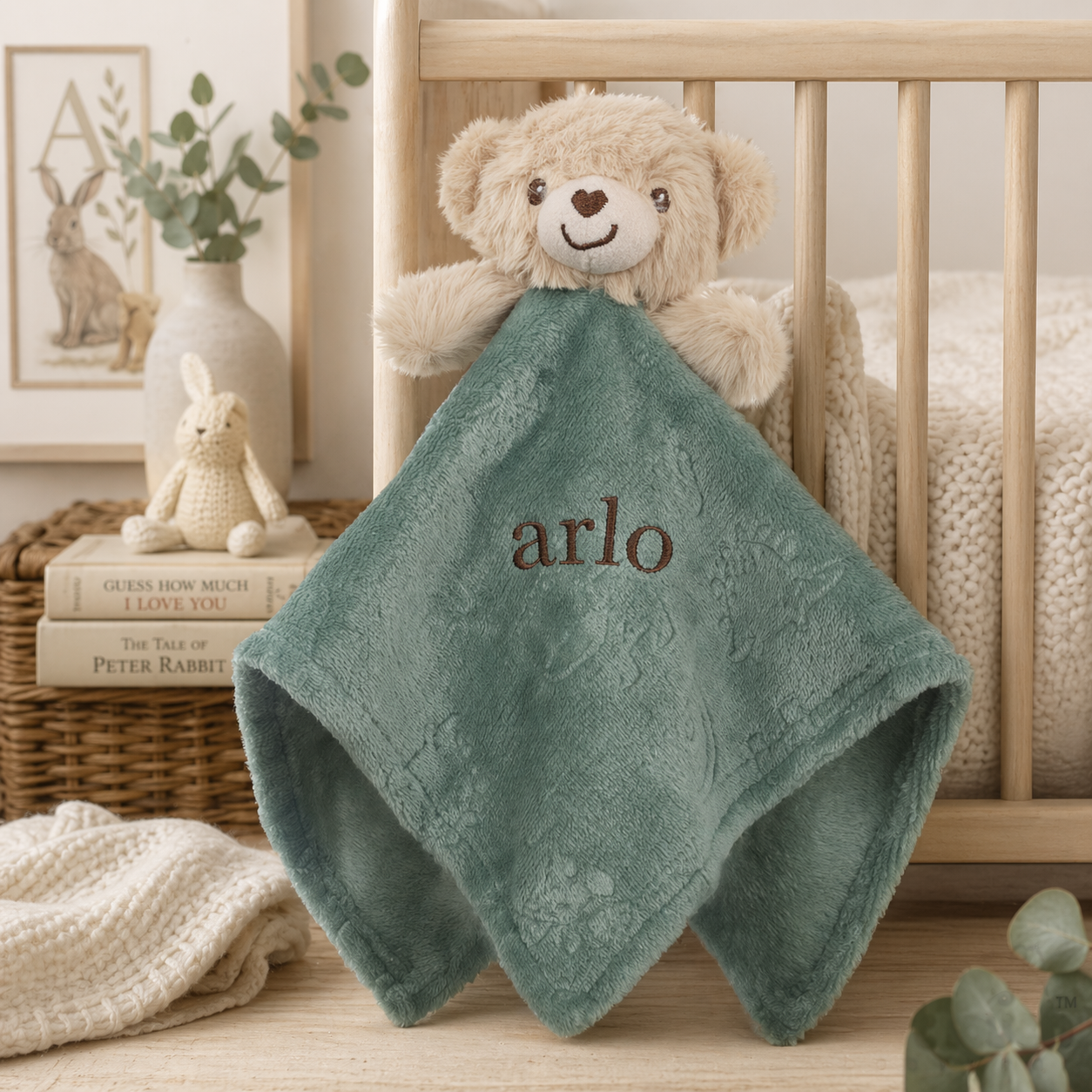 Green baby blanket with 'arlo' embroidered on it, draped over a teddy bear in a crib.