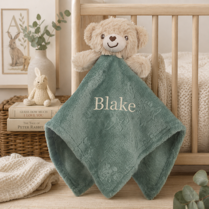 Green baby blanket with 'Blake' embroidered, teddy bear, and books in a crib setting.