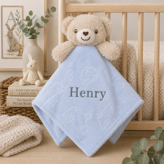 Blue baby blanket with 'Henry' embroidered on it, sitting on a wooden crib in a nursery.
