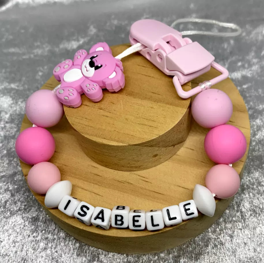 Pink teddybear dummy clip on a grey textured surface. Personalised with the name 'Isabelle'. Change of name is available in the personalisation box. MAM Adapters are available too.