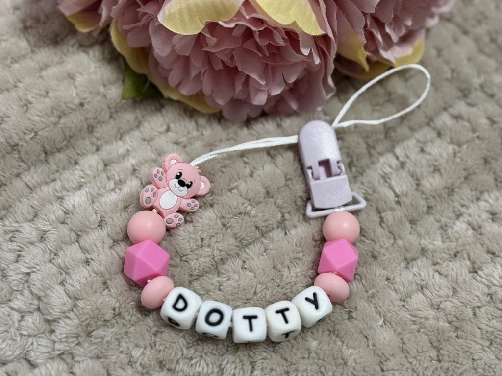 Pink teddybear dummy clip on a beige textured surface with flowers at the top. Personalised with the name 'Dotty'. Change of name is available in the personalisation box. MAM Adapters are available too.