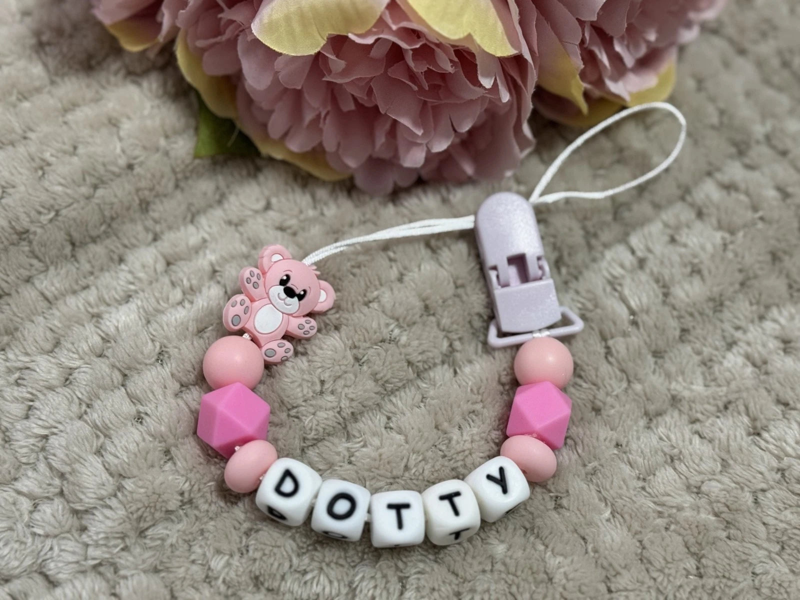 Pink teddybear dummy clip on a beige textured surface with flowers at the top. Personalised with the name 'Dotty'. Change of name is available in the personalisation box. MAM Adapters are available too.
