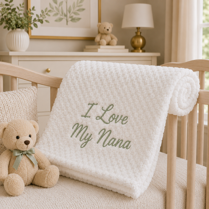 Soft white bubble baby blanket embroidered with "I Love My Nana" in sage green, beautifully styled over a wooden crib in a neutral nursery. A thoughtful keepsake gift for a new baby, baby shower or Nana.